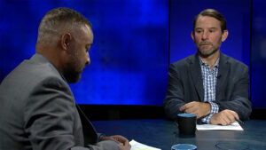 Two men sitting at a table talking to each other.