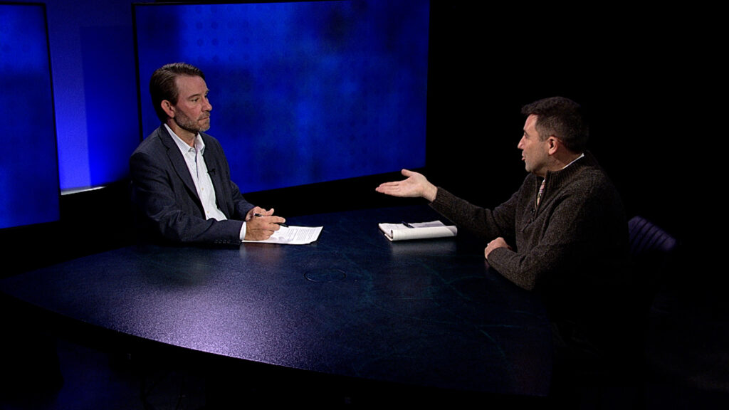 Two men sitting at a table talking to each other.