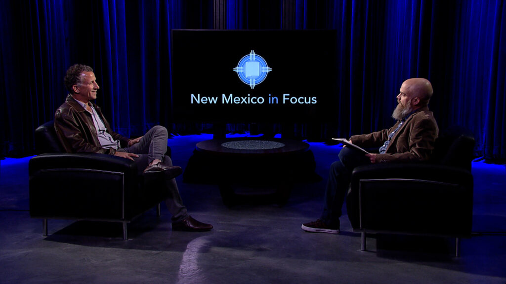 Two men sitting in chairs in front of a screen with the words new mexico's faces.