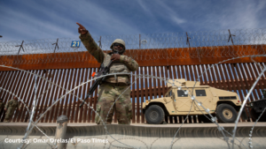 A soldier points to a barbed wire fence at the us-mexico border.