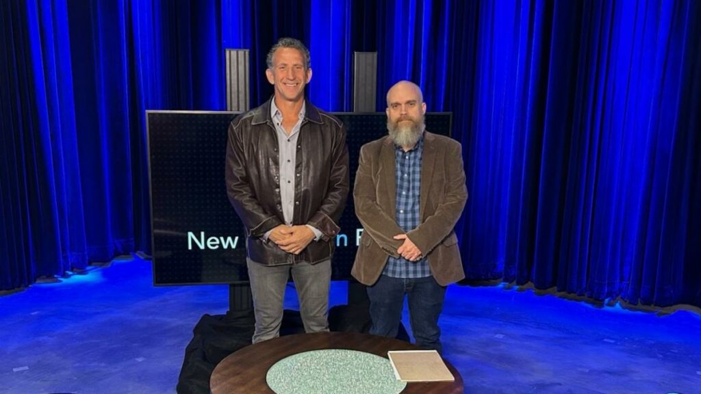 Two men standing in front of a blue screen.