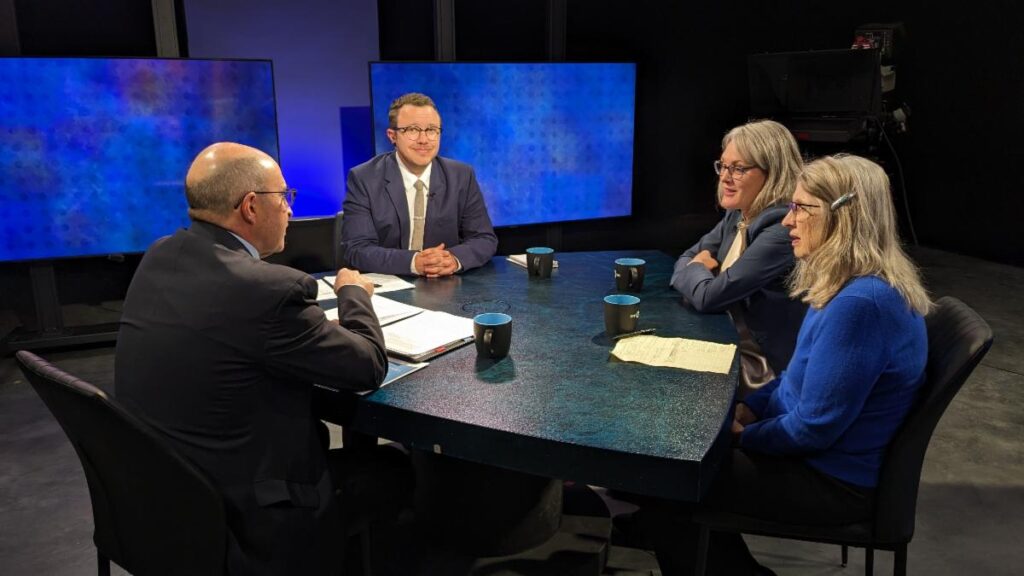 Four people sitting around a table in a television studio.