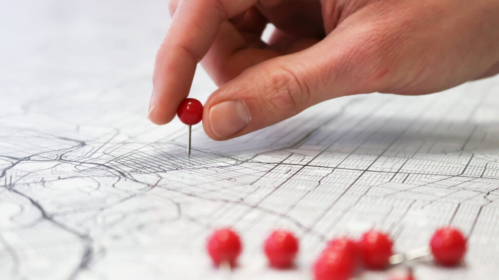 A hand pointing at a map with red pins.