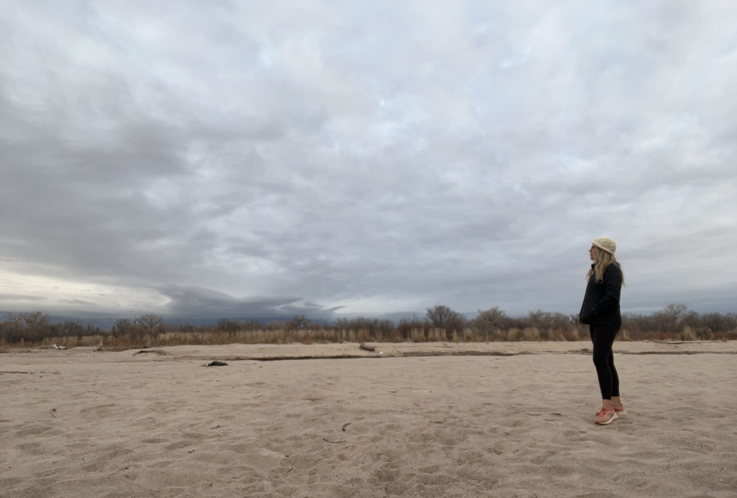 A woman enjoying the serene beauty of a sandy beach under a cloudy sky.