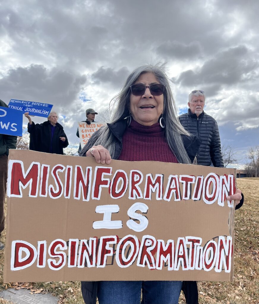 A woman holding up a sign that says misinformation is disinformation, standing near water.