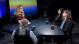 Three people sitting around a table in front of a television.