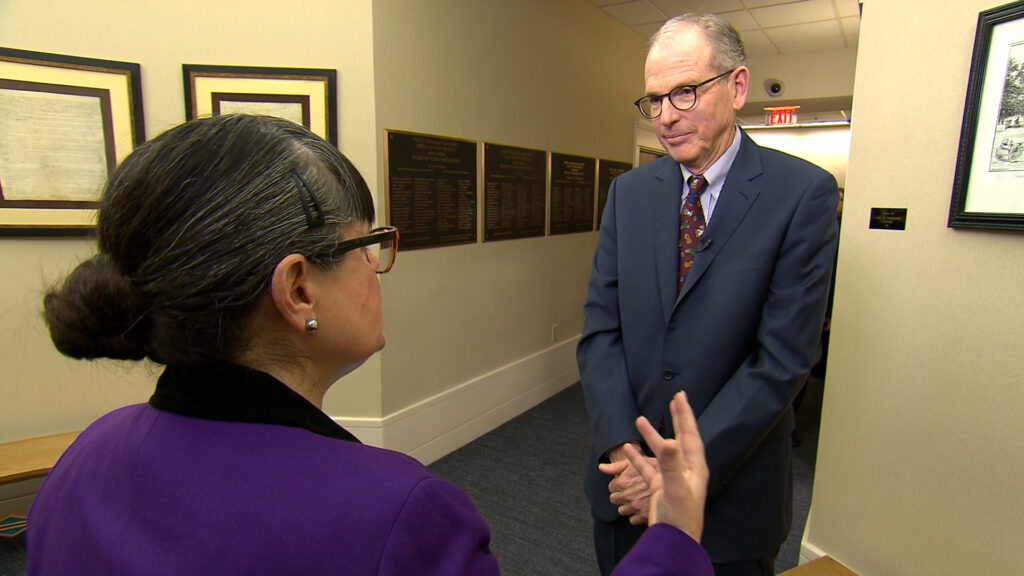 A man in a suit talking to a woman in a hallway.