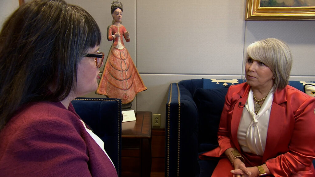 A woman in a red jacket is talking to a woman in a blue jacket.