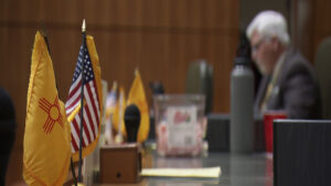 A man sits at a desk with flags in front of him.