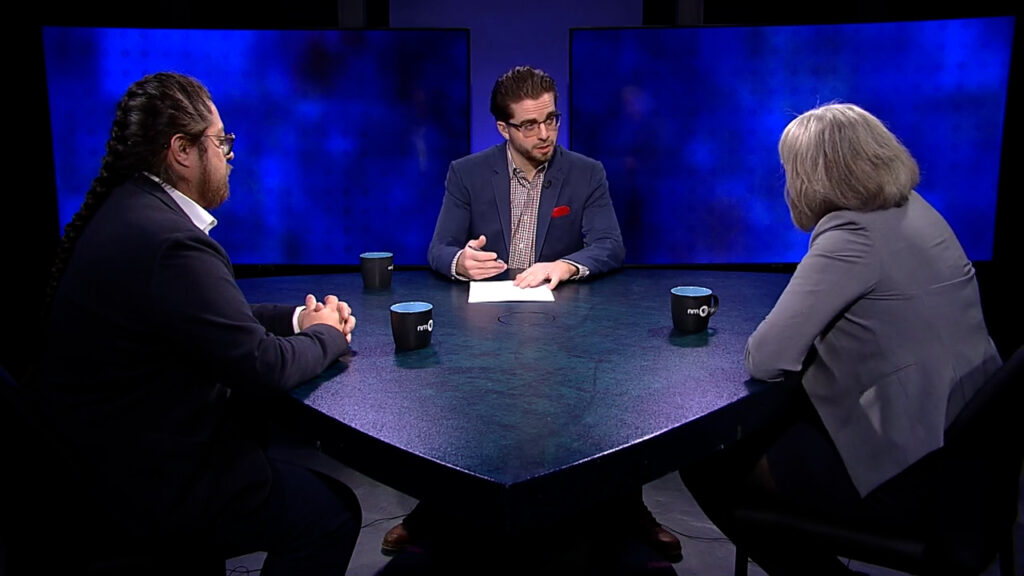 Three people sitting at a table in front of a blue screen.