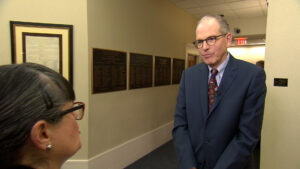 A man in a suit and tie talking to a woman in a hallway.