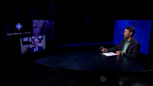 A man sits at a table in front of two televisions.