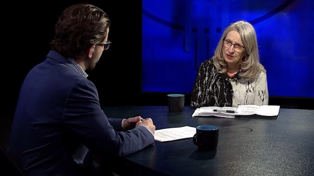 Two individuals engaged in a conversation on a tv set with a blue backdrop.