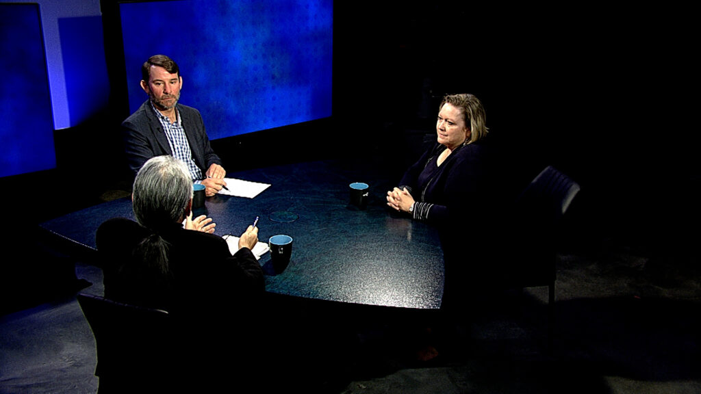 Three people engaged in a discussion at a round table in a studio setting.