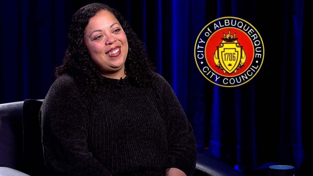 Woman smiling during an interview, with the city of albuquerque city council seal in the background.