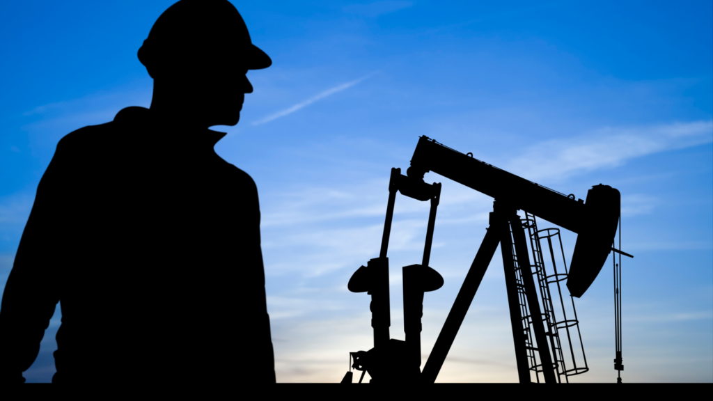 Silhouette of a worker observing oil pumpjacks at dusk.