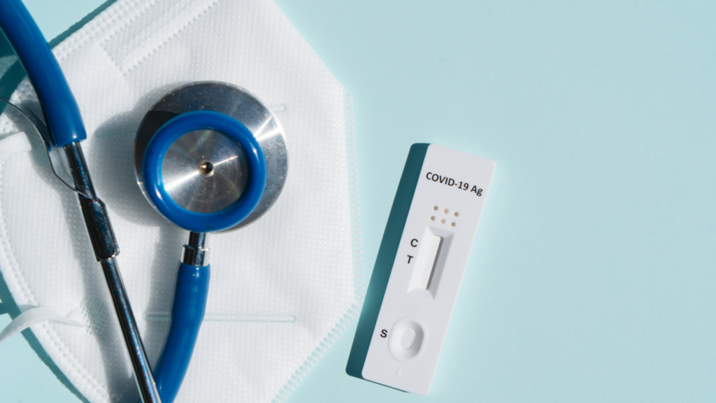 A covid-19 rapid antigen test alongside a stethoscope and a protective mask on a light blue background.