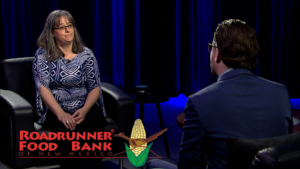 Two individuals engaged in an interview setup, with the logo of roadrunner food bank of new mexico displayed in the foreground.