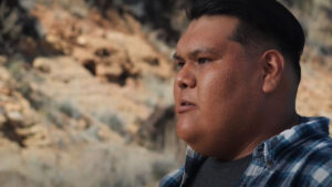 A man in a plaid shirt outdoors with a thoughtful expression.