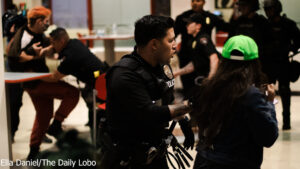 Police officer interacting with a civilian in a crowded indoor space, with other officers and individuals in the background.