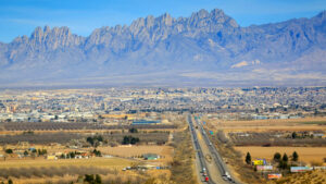 Aerial view of a busy highway leading towards a city with rugged mountains in the background under a clear sky.