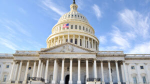 Image of the United States Capitol building with a U.S. flag flying in front of it, showcasing its iconic dome and neoclassical architectural style on a clear day.