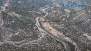 Aerial view of a winding river cutting through a mountainous landscape, surrounded by dense vegetation and rocky terrain. The vibrant blue water adds a striking contrast to the green and gray tones. LightHawk logo is visible in the top right corner.