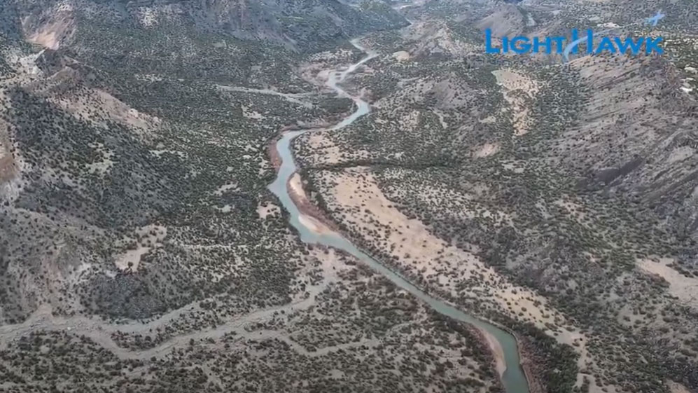 Aerial view of a winding river cutting through a mountainous landscape, surrounded by dense vegetation and rocky terrain. The vibrant blue water adds a striking contrast to the green and gray tones. LightHawk logo is visible in the top right corner.