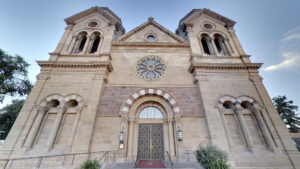 Stone cathedral facade with arched door, round stained glass window above, and twin towers on either side, viewed from the front.