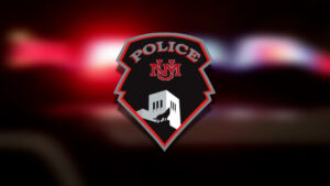 A police badge with "Police NM" and a building with a wolf image, set against a blurred background of red and blue lights.