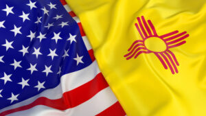 The United States flag and the New Mexico state flag are shown side by side, both flags appear to be gently waving.