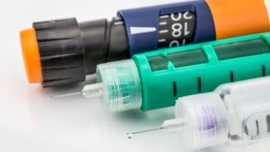 Close-up of three insulin pens with needles exposed, showing different colors and dose dials, placed side by side on a white surface.
