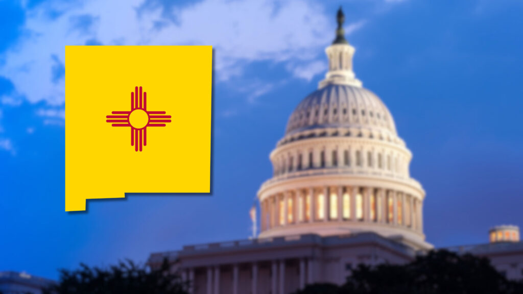 The New Mexico state flag in the shape of the state is shown next to the U.S. Capitol building at dusk.