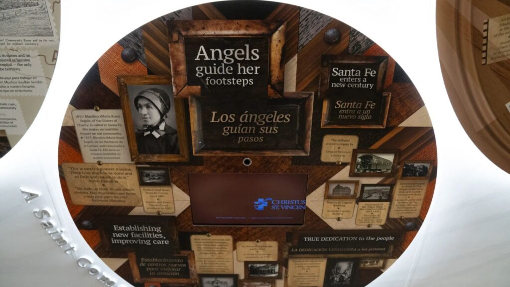 A round display features historical photos, text panels about Santa Fe and healthcare, and a central screen labeled “CHRISTUS ST. VINCENT.”.