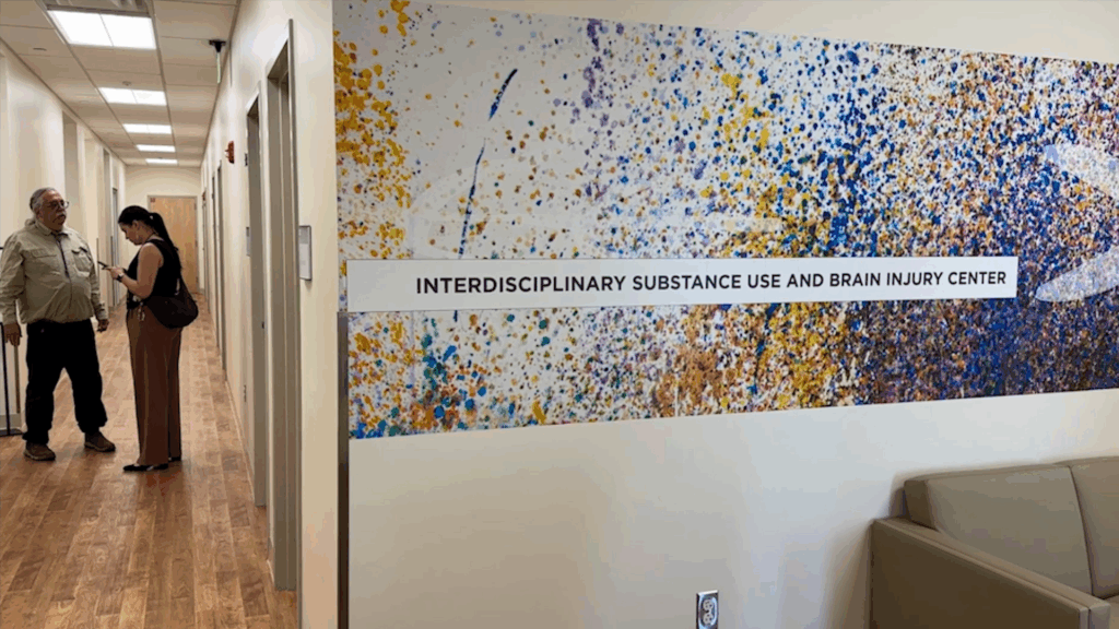 Hallway with two people talking and a wall mural that reads "Interdisciplinary Substance Use and Brain Injury Center" in a medical or academic facility.