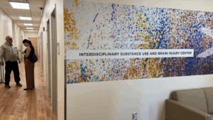 Hallway with two people talking and a wall mural that reads "Interdisciplinary Substance Use and Brain Injury Center" in a medical or academic facility.