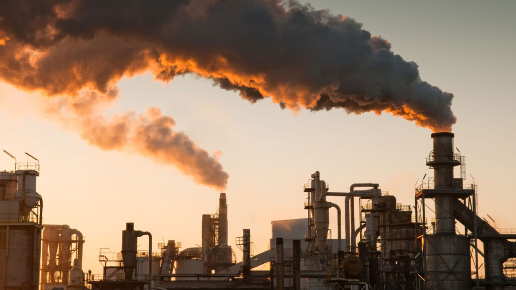 Industrial facility emitting large plumes of smoke from tall chimneys against the evening sky.