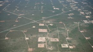 Aerial view of a landscape with numerous oil well pads, intersecting roads, and sparse vegetation.