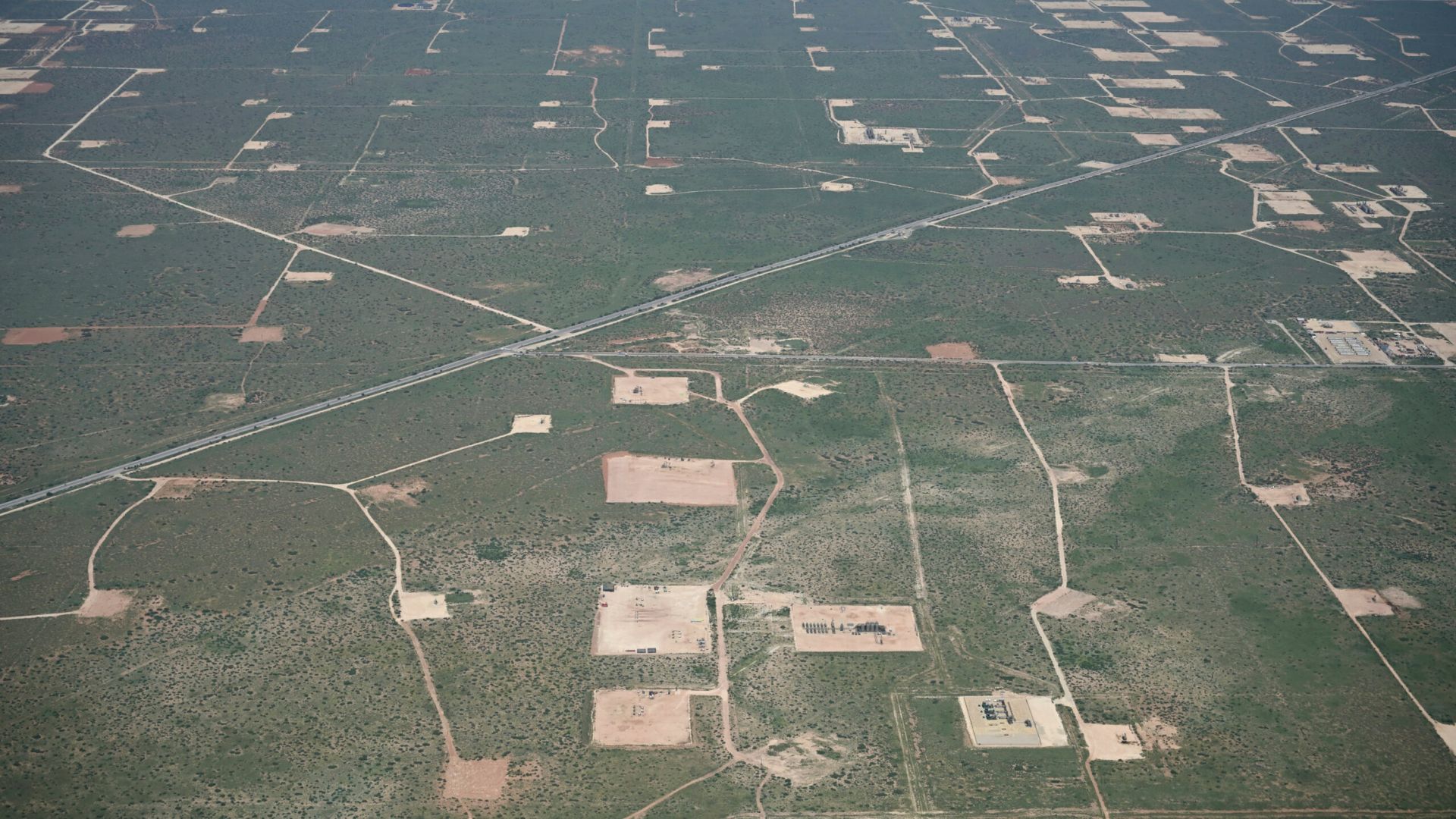 Aerial view of a landscape with numerous oil well pads, intersecting roads, and sparse vegetation.