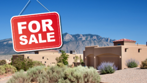 A red "For Sale" sign is shown in front of a Southwestern-style house with mountains in the background under a clear blue sky.