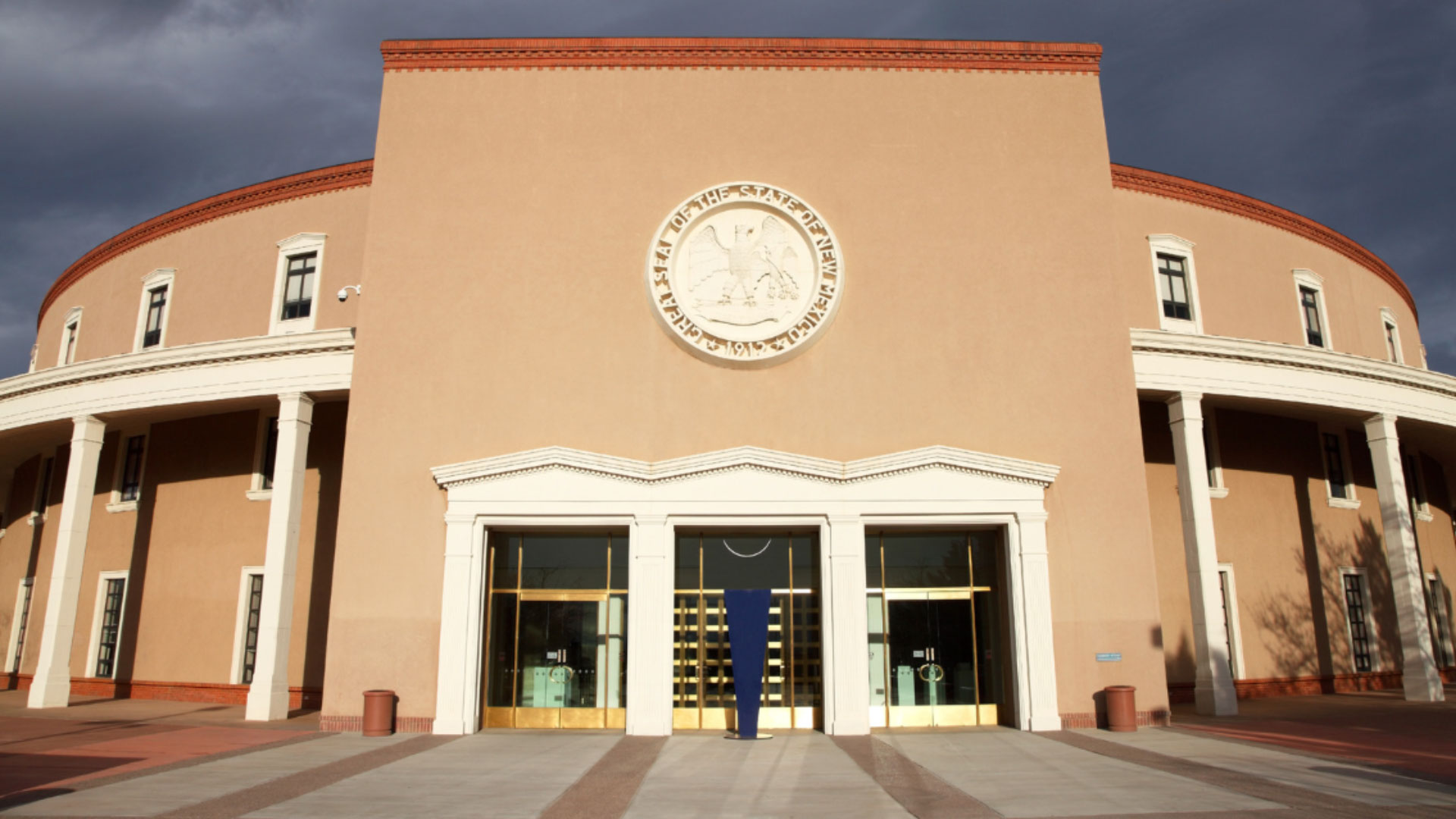 Front view of the New Mexico State Capitol building with a large state seal above the main entrance and columns on each side.