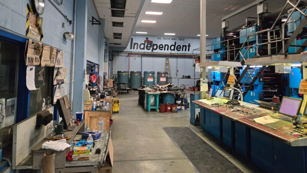 Interior of an industrial workshop with workstations, blue cabinets, tools, and various equipment scattered across tables and shelves. A sign reads "Independent" at the far end.