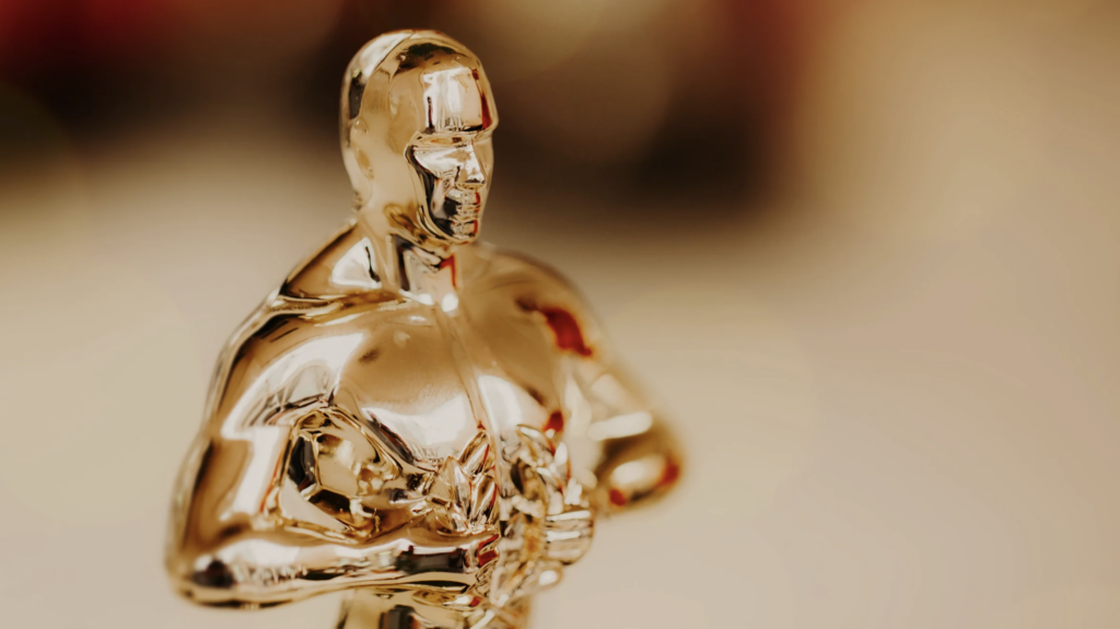 Close-up of a gold Oscar statuette against a blurred, neutral background.