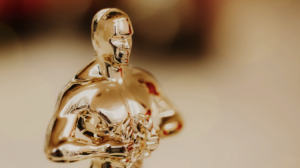 Close-up of a gold Oscar statuette against a blurred, neutral background.