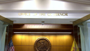 Entrance to the Office of the Governor with a state seal, American flag, and New Mexico state flag visible inside.