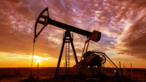 An oil pumpjack operates in a field at sunset under a partly cloudy sky.
