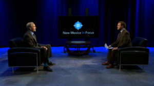 Two men in suits sit across from each other in a TV studio with "New Mexico in Focus" displayed on a screen between them.