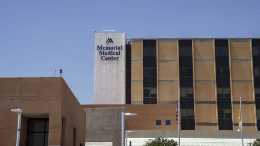 The exterior of Memorial Medical Center shows a multi-story building with the facility’s name and logo visible on the upper facade.