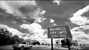 A road sign reads "Roswell City Limits, Elev. 3570." Nearby, a pickup truck drives while a large, saucer-shaped object floats in the sky.
