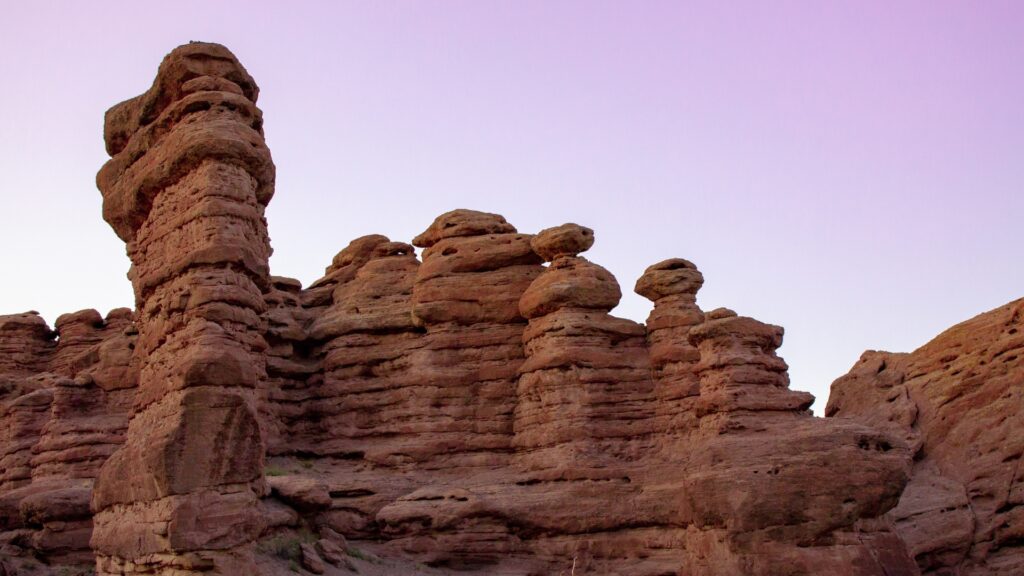 Tall red sandstone rock formations against a pale purple sky.